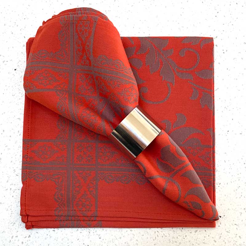 Orange patterned napkin with a silver napkin ring on a white background