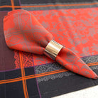 Orange patterned napkin with a gold napkin ring on a tablecloth.