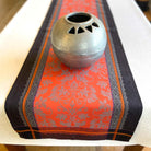 Decorative table runner with intricate patterns and a metallic pot on top