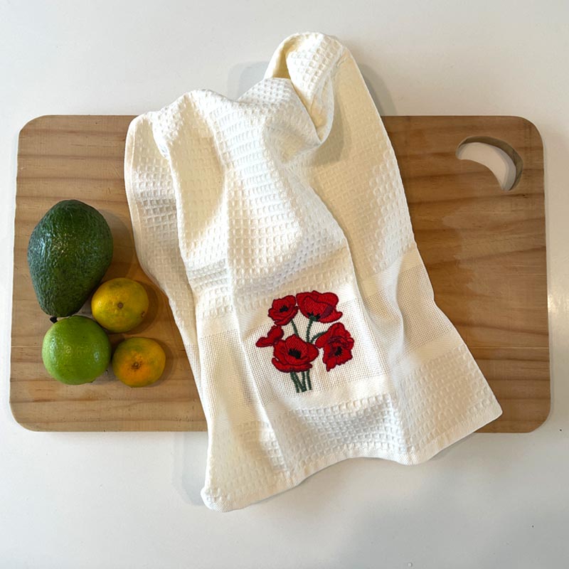 White towel with red floral design on a wooden cutting board with fruits