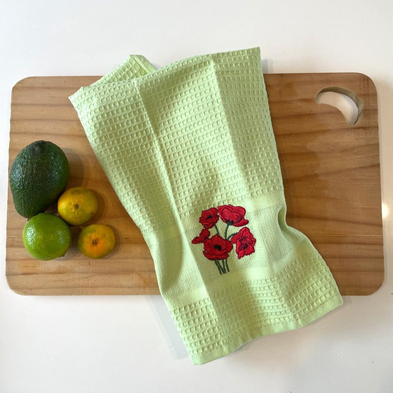 Green towel with floral embroidery on a wooden cutting board with fruits