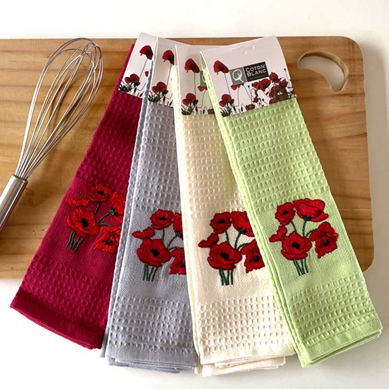 Four kitchen towels with floral design on a wooden cutting board with a whisk.