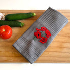Gray towel with red floral embroidery on a wooden surface with vegetables.
