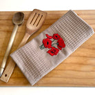 Beige towel with red floral embroidery on a wooden surface with wooden spoon and spatula.