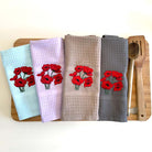 Four kitchen towels with red floral designs on a wooden board.
