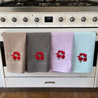 Four kitchen towels with red flower designs hanging on a stove.