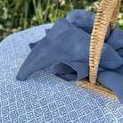 Blue fabric draped over a wicker basket on a patterned surface with greenery in the background