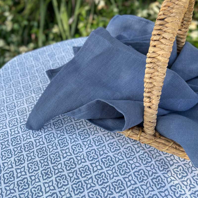 Blue fabric draped over a wicker basket on a patterned surface with greenery in the background