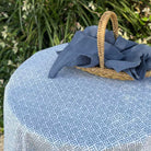 Blue fabric draped over a woven basket on a patterned tablecloth with greenery in the background