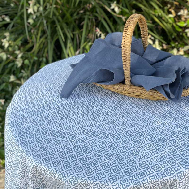 Blue fabric draped over a woven basket on a patterned tablecloth with greenery in the background
