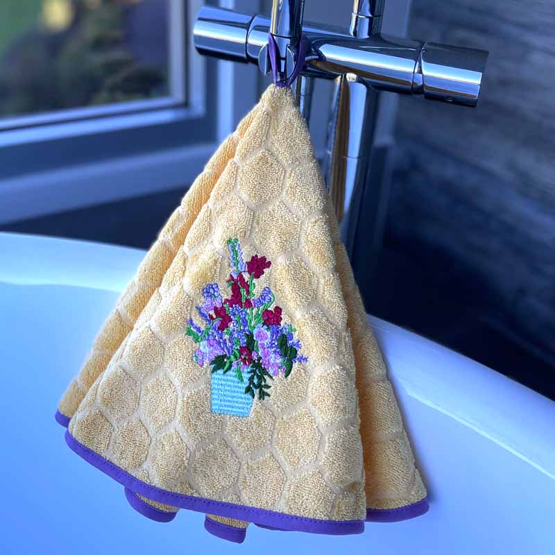 Yellow hanging towel with embroidered flower design hanging on a faucet