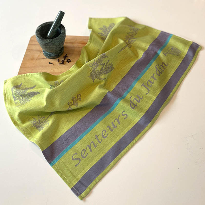 Green towel with garden-themed design on a wooden board with a mortar and pestle.