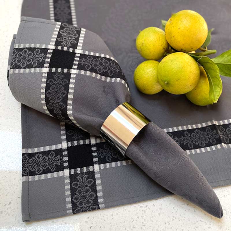 Gray checkered napkin with decorative patterns, silver napkin ring, and lemons on a white surface